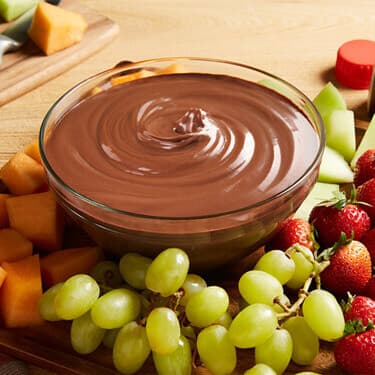 A glass bowl of chocolate vanilla dessert surround by grapes and strawberries. 